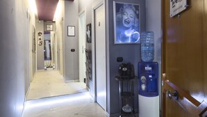 Een hotelgang met een waterdispenser, een koffieapparaat en een ingelijst kunstwerk aan de muur.