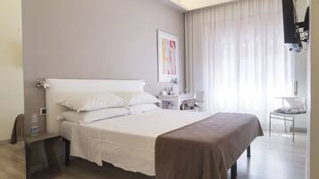 A hotel room with a large bed, a bedside table, a chair, and a TV mounted on the wall.