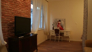 A room with a brick wall, a television on a wooden cabinet, a desk with a chair, and a painting on the wall. - Banica Apartments & Rooms (Split)