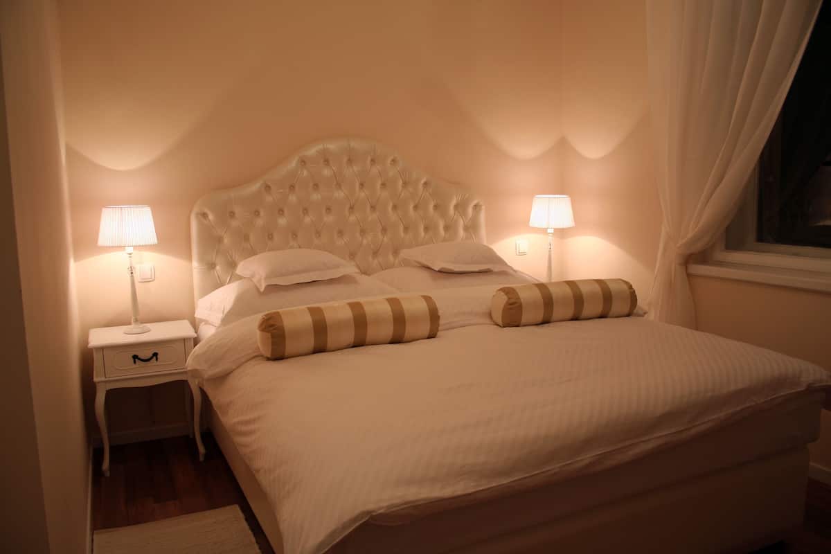 A neatly made bed with a tufted headboard, two bedside tables with lamps, and a window with curtains.