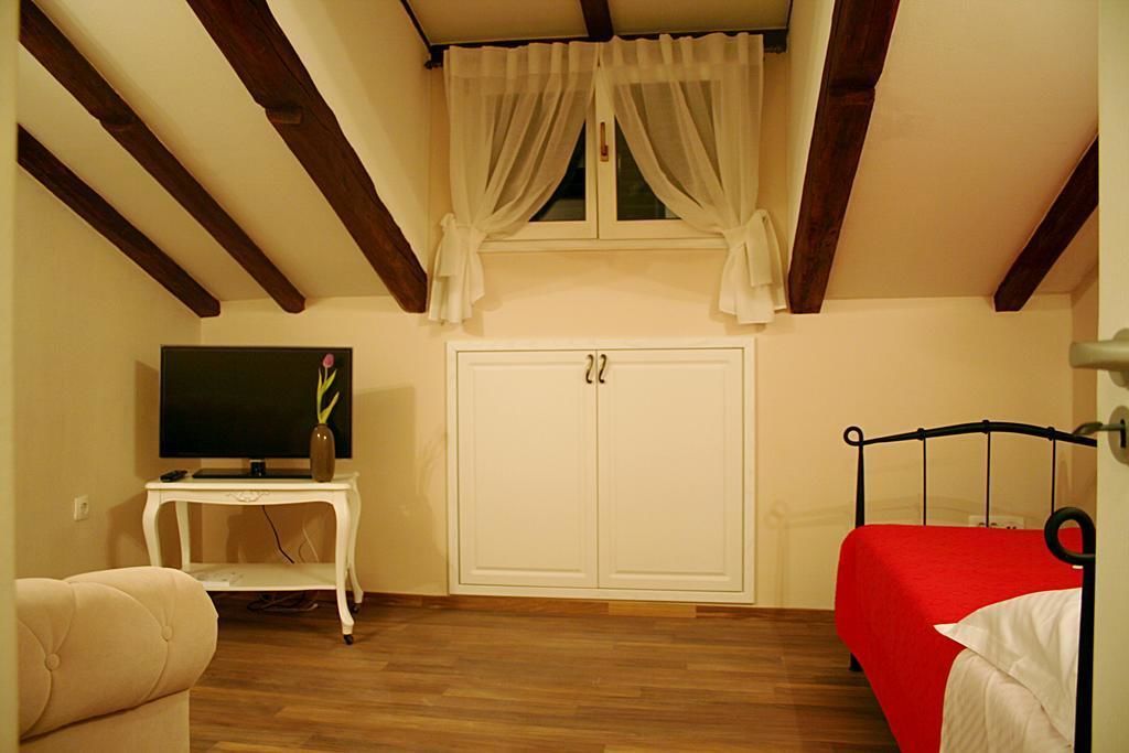 Een slaapkamer met een houten plafond, een televisie op een klein tafeltje, een kast en een bed met een rode spreidek.