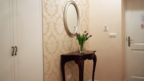 A hallway with a patterned wallpaper, a mirror, a small table with a vase of flowers, and a door with a sign. - Banica Apartments & Rooms (Split)