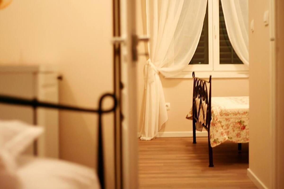 A bedroom with a bed, a chair, a window with curtains, and a radiator.