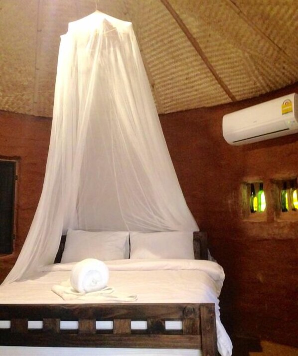 Una cama con dosel, un aire acondicionado instalado en la pared y un ventanal con vidrio esmerilado.