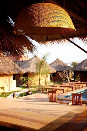 A poolside area with wooden lounge chairs and thatched-roof huts in the background. - Korawan Garden View (Hua Hin)