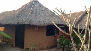 A thatched-roof hut with a small window, surrounded by a garden with stepping stones and potted plants. - Korawan Garden View (Hua Hin)