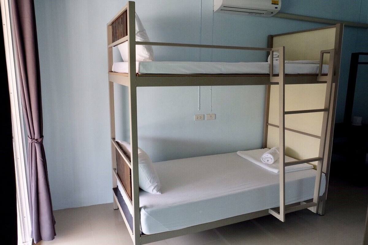 Una cama litera con estructura de madera, un colchón y almohadas. Hay un equipo de aire acondicionado encima de la cama.