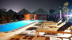 A swimming pool with lounge chairs and thatched-roof huts. - Korawan Garden View (Hua Hin)