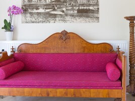 A wooden sofa with a red upholstered seat and matching cushions, positioned against a wall with a black and white cityscape painting.