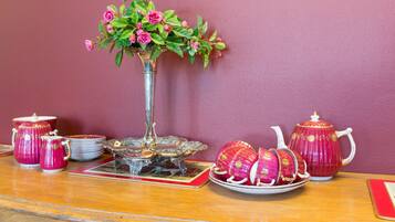 A table with a vase of pink roses, a teapot, and several cups and saucers.