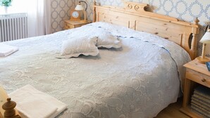 Una cama bien tendida con una colcha estampada, un cabecero de madera y una mesita de noche con una lámpara y libros.