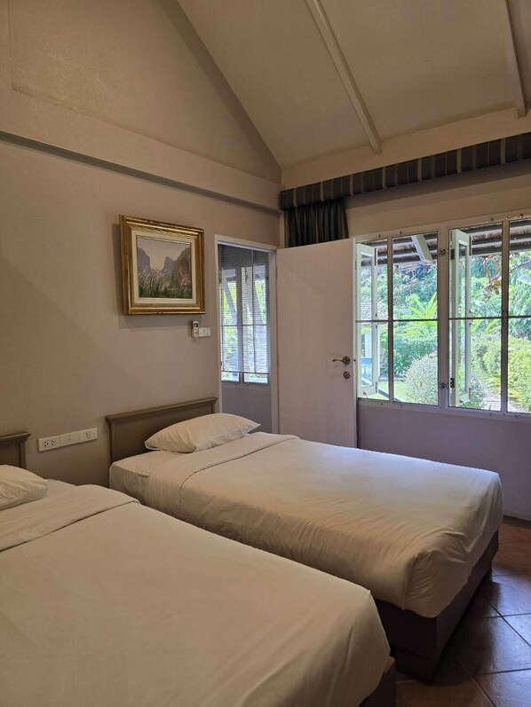 Una habitación con dos camas, un cuadro en la pared y una ventana con vistas a zonas verdes.