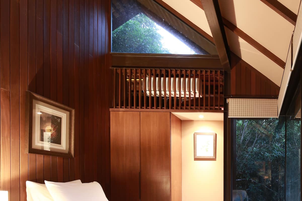A bedroom with a large bed, wooden walls, and a window overlooking greenery.
