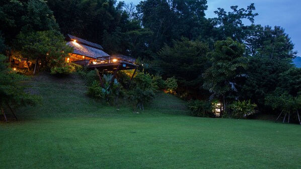 A house with a sloped roof and a wooden deck, surrounded by lush greenery and trees.