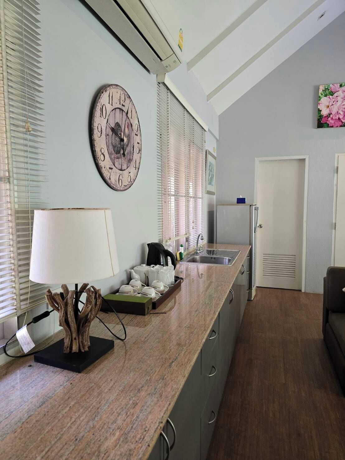 A kitchen with a wooden clock, a sink, and a countertop with kitchen items.