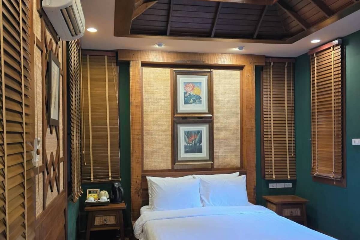 A bedroom with a wooden bed, a nightstand, a wall-mounted air conditioner, and framed artwork.