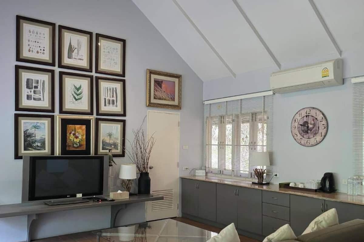 A modern living room with a large flat-screen TV, a sofa, a coffee table, and a kitchen area with a window and blinds.