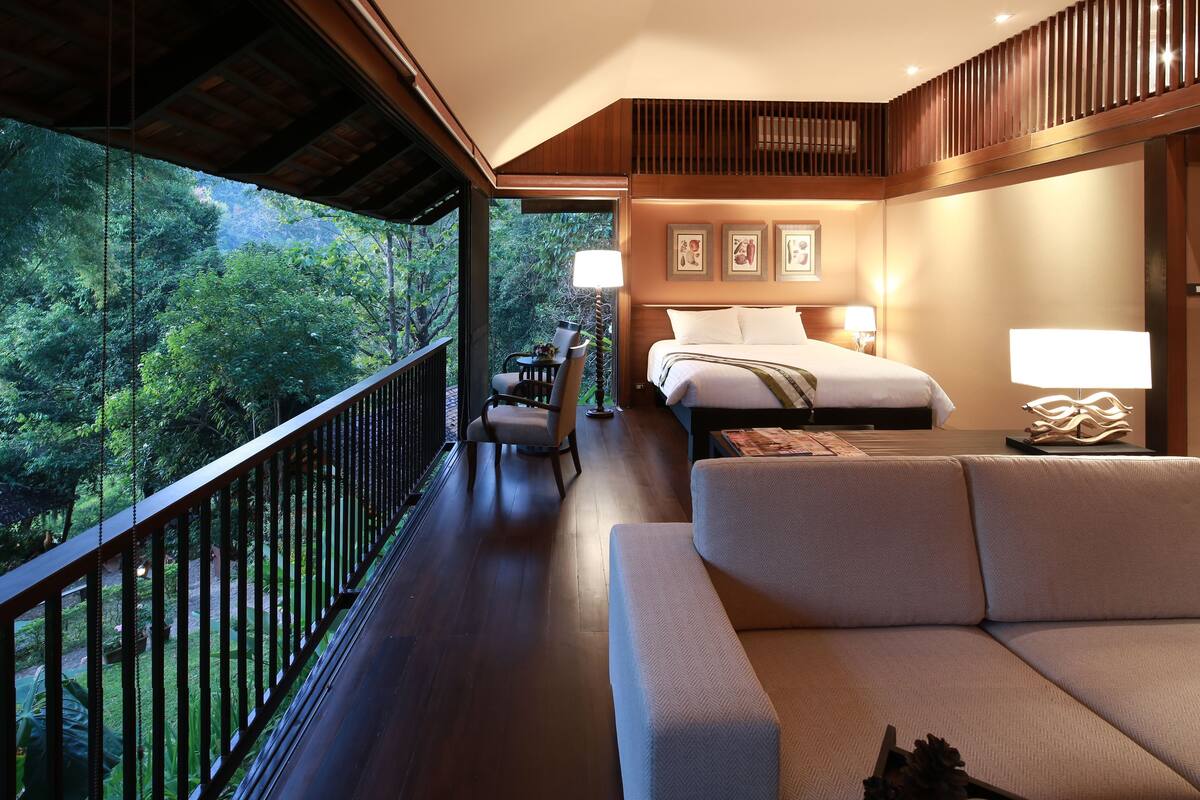 A spacious balcony with a wooden railing, a bed with white linens, a sofa, and a dining table set with cups and saucers.