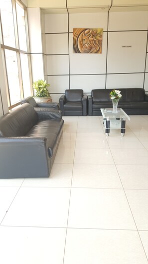 Eine moderne Lobby mit einer schwarzen Ledersofa, einem Glastisch und einer Topfpflanze.