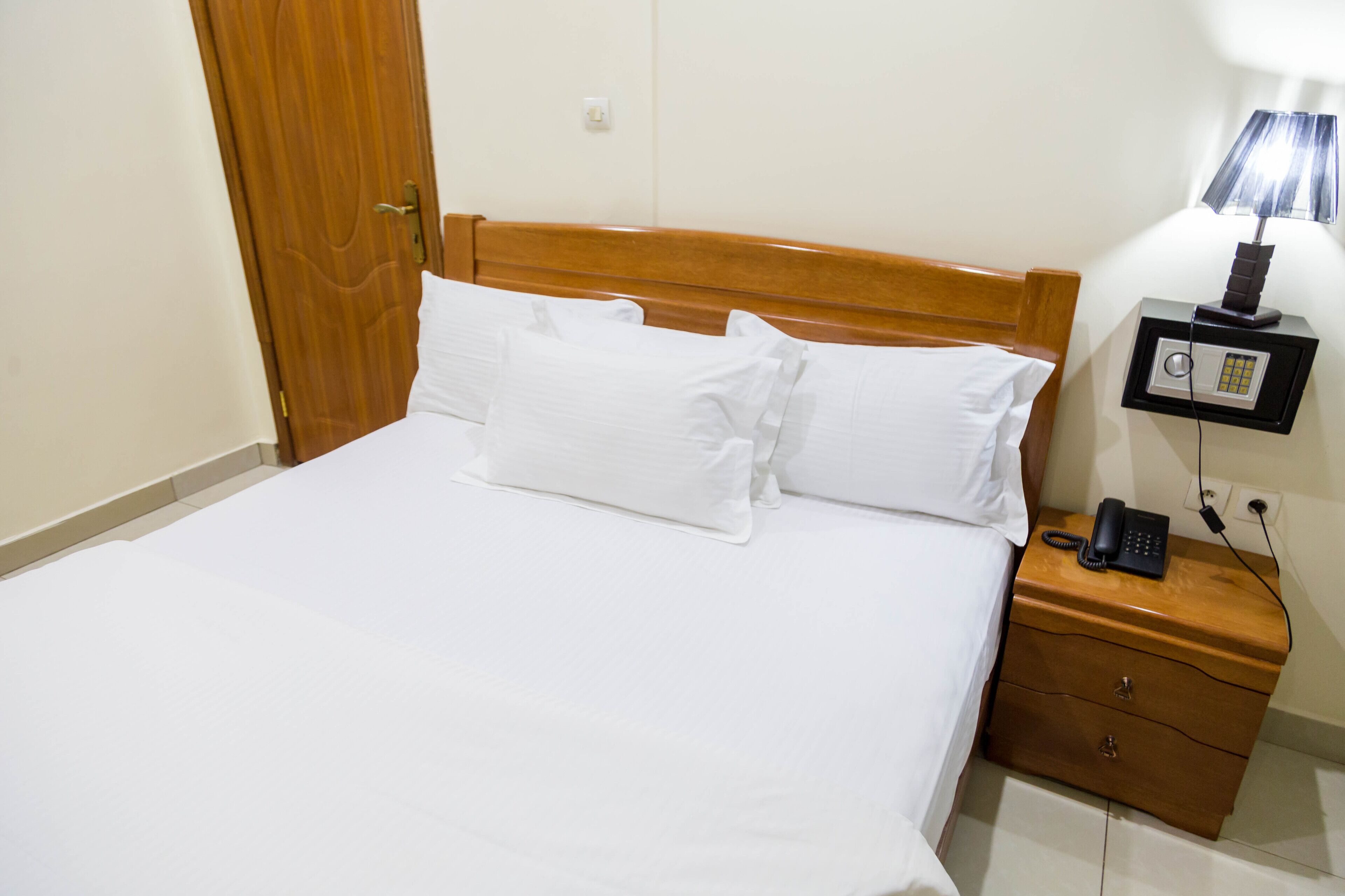 A hotel room with a wooden headboard, a bed with white linens, a bedside table with a lamp, and a phone.