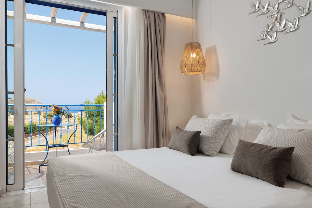 Un dormitorio con cama, almohadas, una lámpara colgante y vistas al exterior.