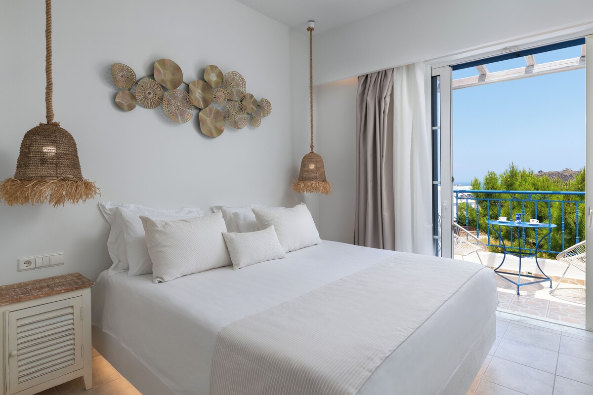 A bedroom with a large bed, a wall-mounted decorative item, and a view of a balcony with outdoor furniture.