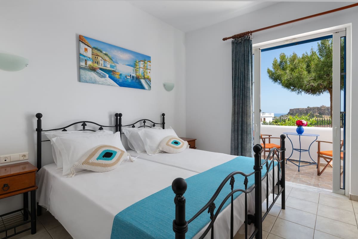 Un dormitorio con cama, mesita de noche, un cuadro y vista al exterior.