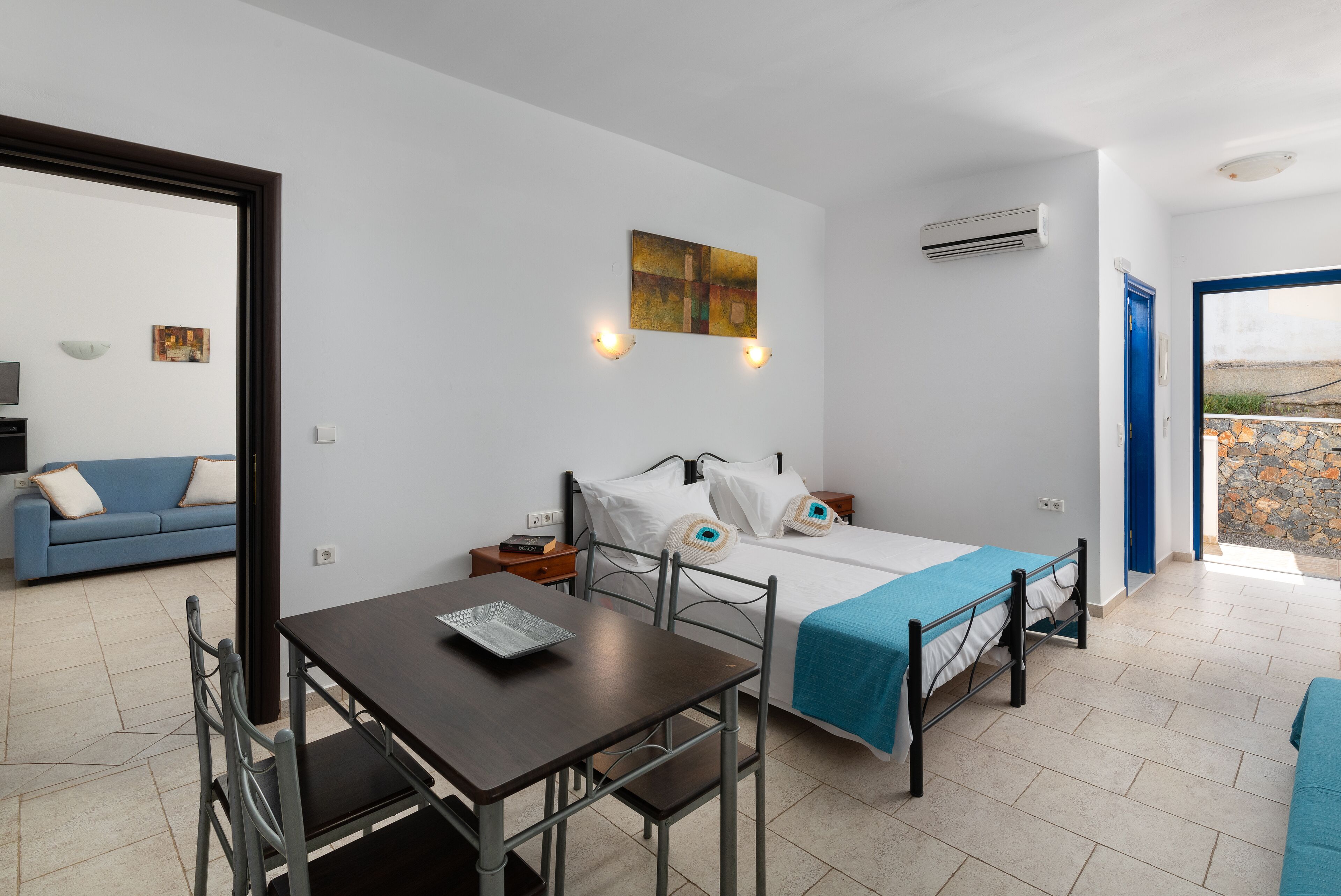 Quarto com uma cama, uma mesa e uma cadeira. Há um quadro na parede e um aparelho de ar condicionado.