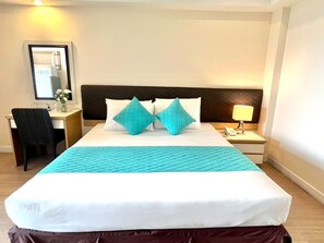 A hotel room with a bed, a desk, a chair, a nightstand with a lamp, and a mirror on the wall. - Sky Place Serviced Apartment (Bangkok)