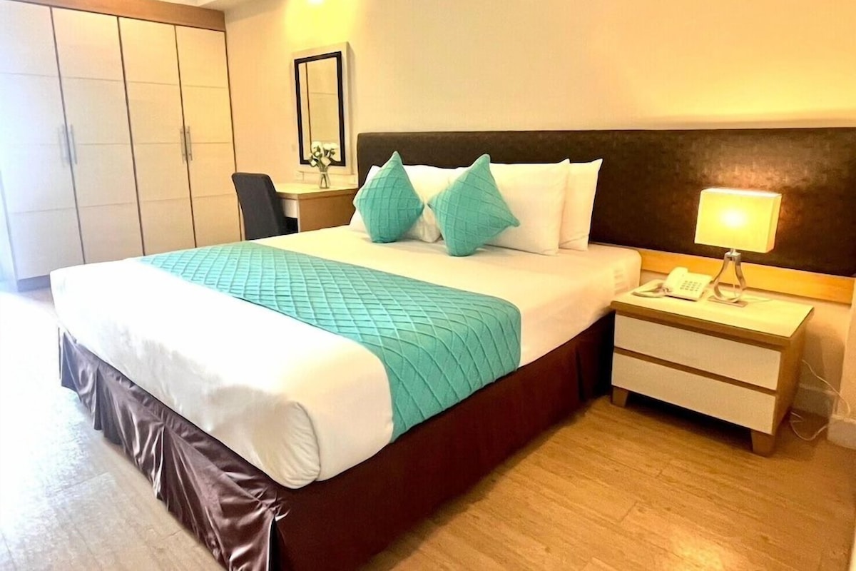 A hotel room with a large bed, a bedside table with a lamp, a phone, and a mirror on the wall.