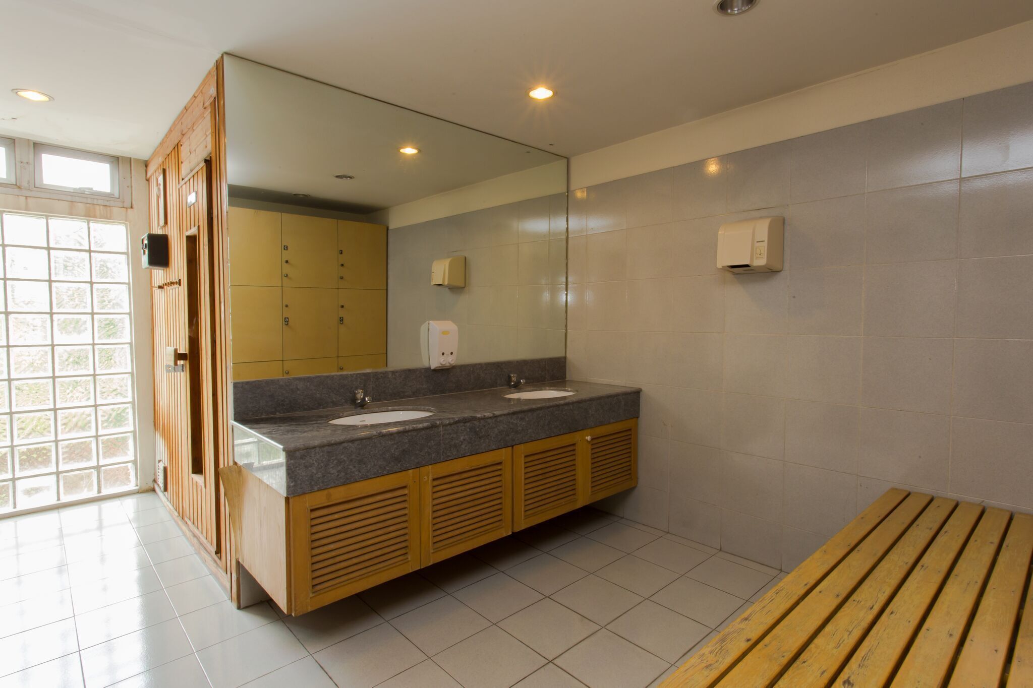 Un baño moderno con dos lavamanos, un espejo grande, armarios de madera y un banco.