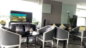 Ein modernes Wohnzimmer mit einem Flachbildfernseher, grau-weißen Möbeln und einem Blick auf einen Garten durch große Fenster.
