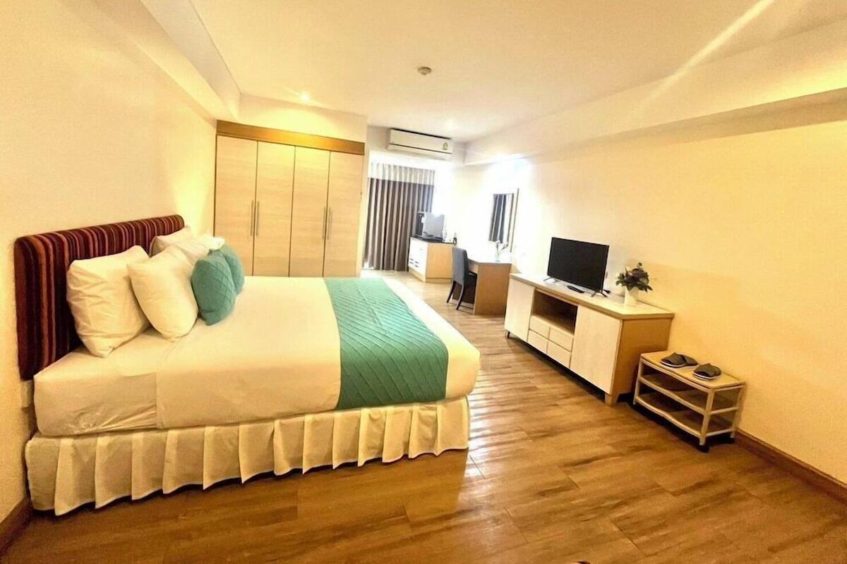 A hotel room with a bed, wardrobe, desk, TV, and a small plant.