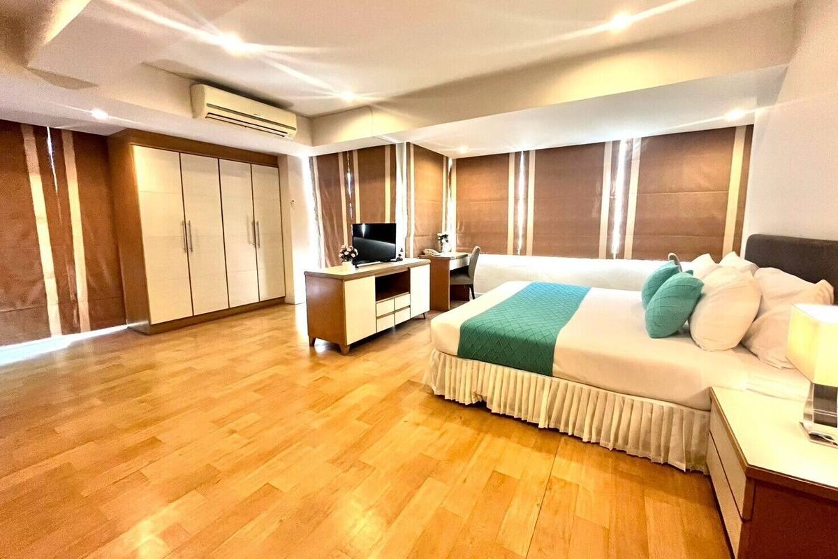 A hotel room with a large bed, a desk with a computer, a TV, and a wardrobe.