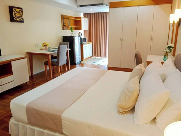 A hotel room with a bed, a desk, a chair, a wardrobe, and a television. - Sky Place Serviced Apartment (Bangkok)