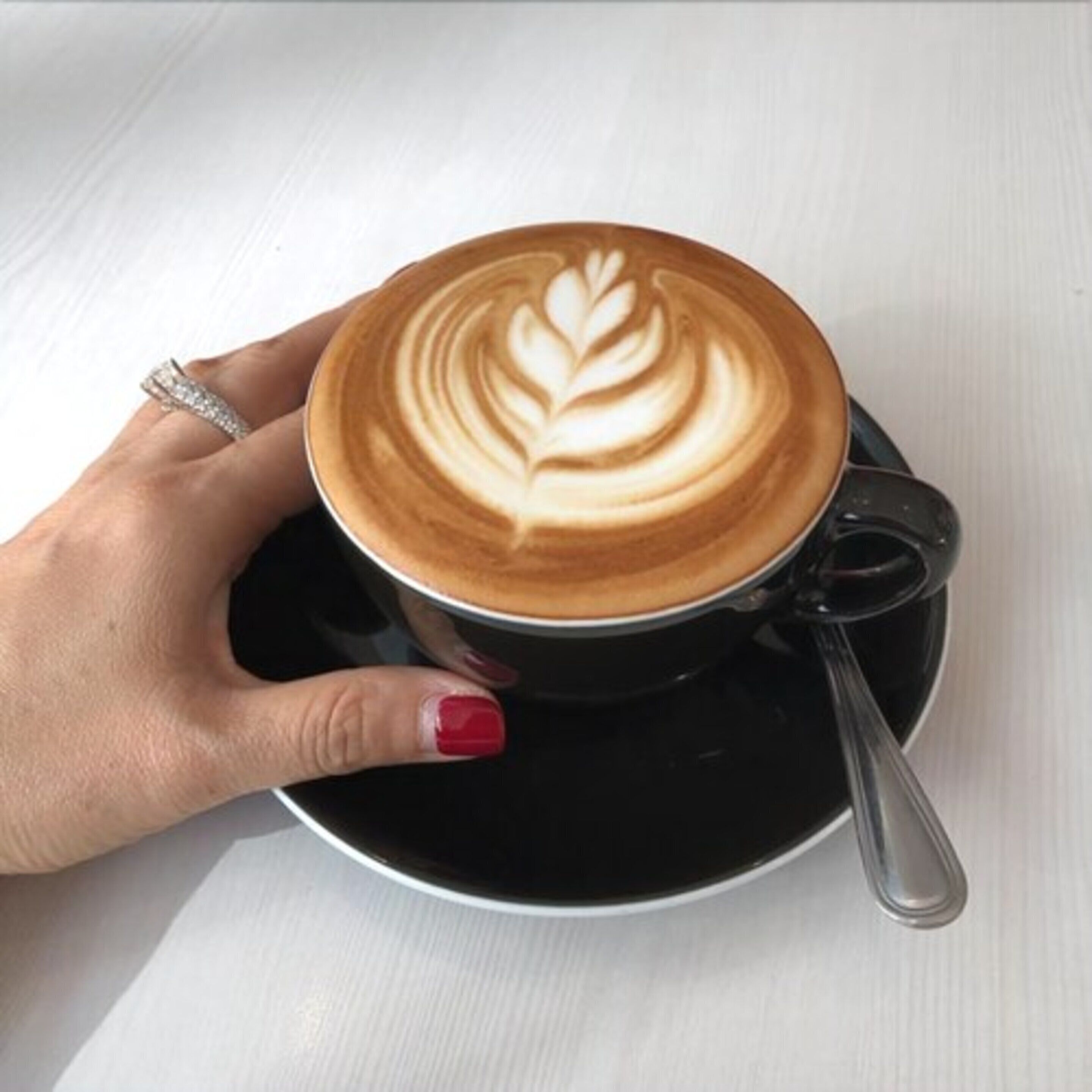 Una mano sosteniendo una taza de café con arte de latte sobre un platillo.