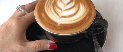 Una mano sosteniendo una taza de café con arte de latte sobre un platillo.