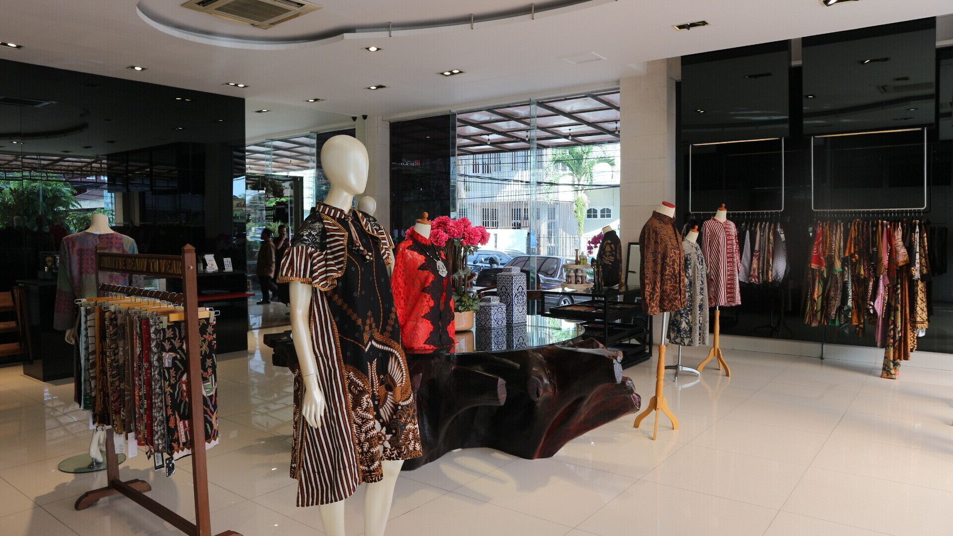 A modern boutique with mannequins displaying clothing, a central seating area, and large windows allowing natural light.