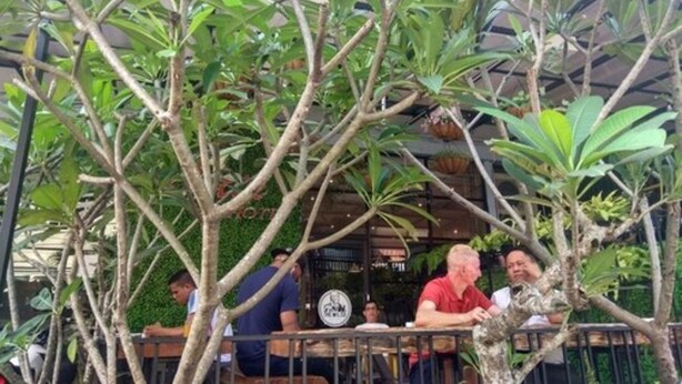 An outdoor seating area with tables and chairs, surrounded by lush greenery and trees. - The Batik Hotel (Medan)