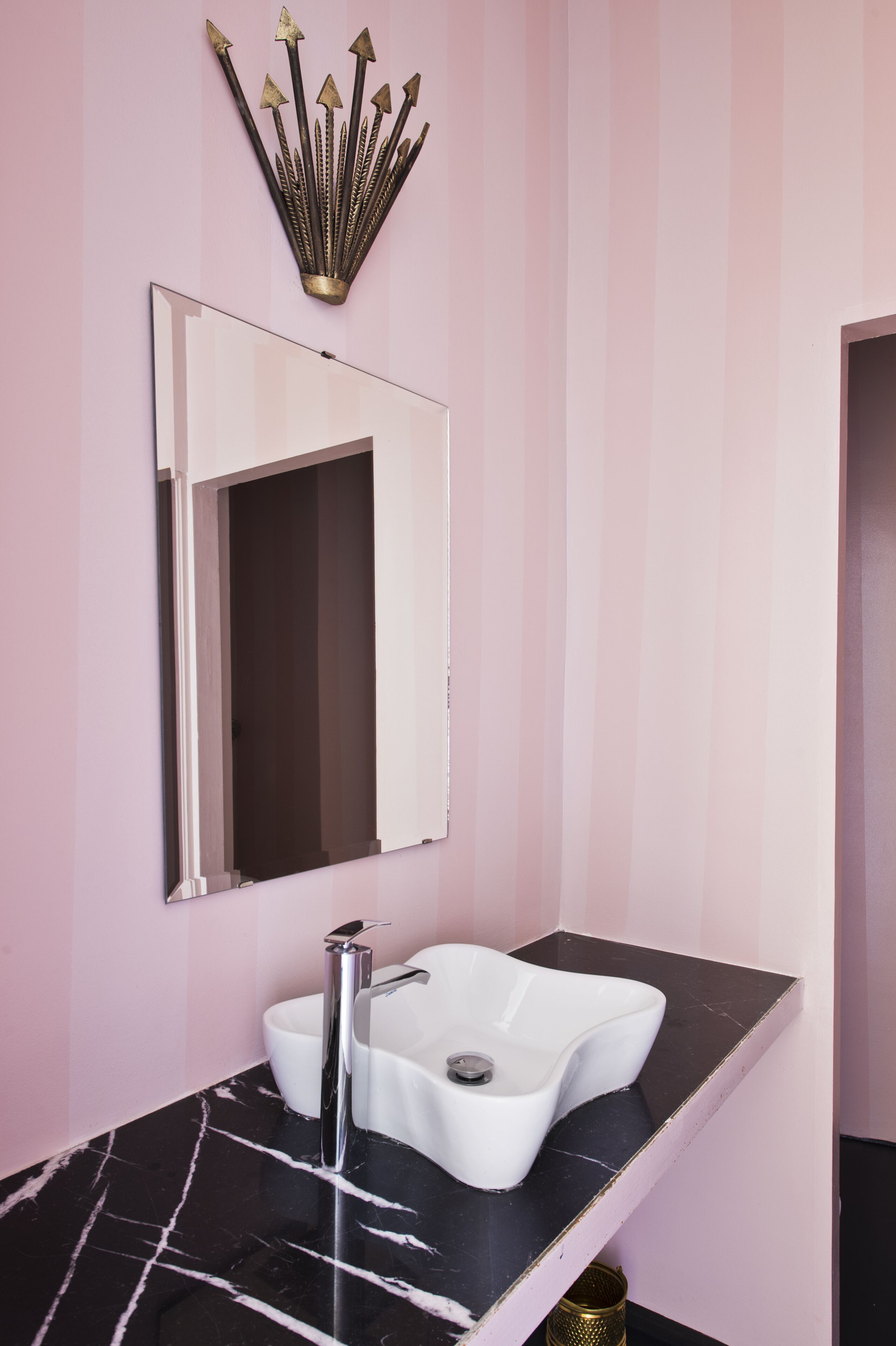 A bathroom with a white sink, black marble countertop, and a gold decorative piece above the mirror.