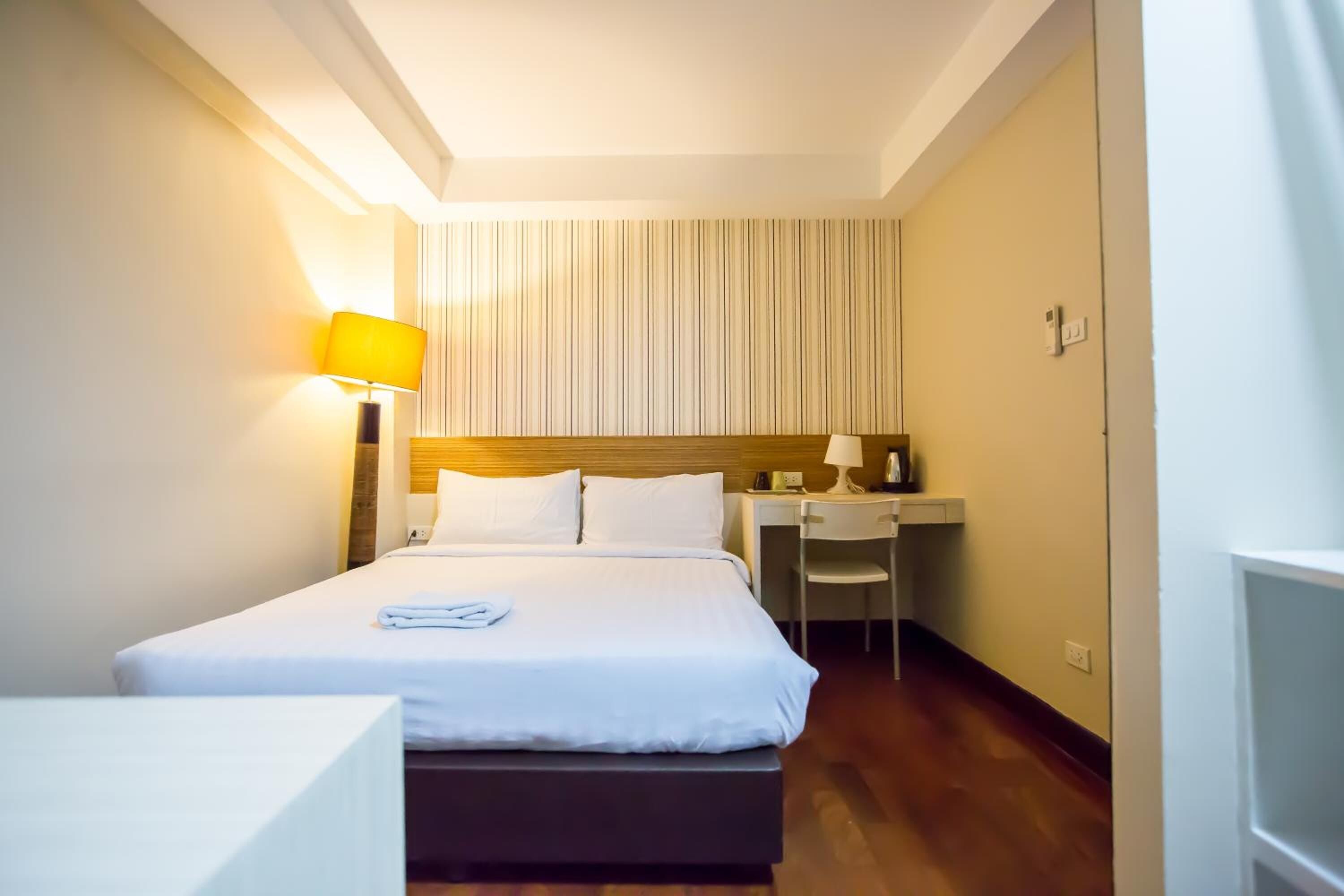 Una habitación de hotel con cama, escritorio, silla y lámpara.