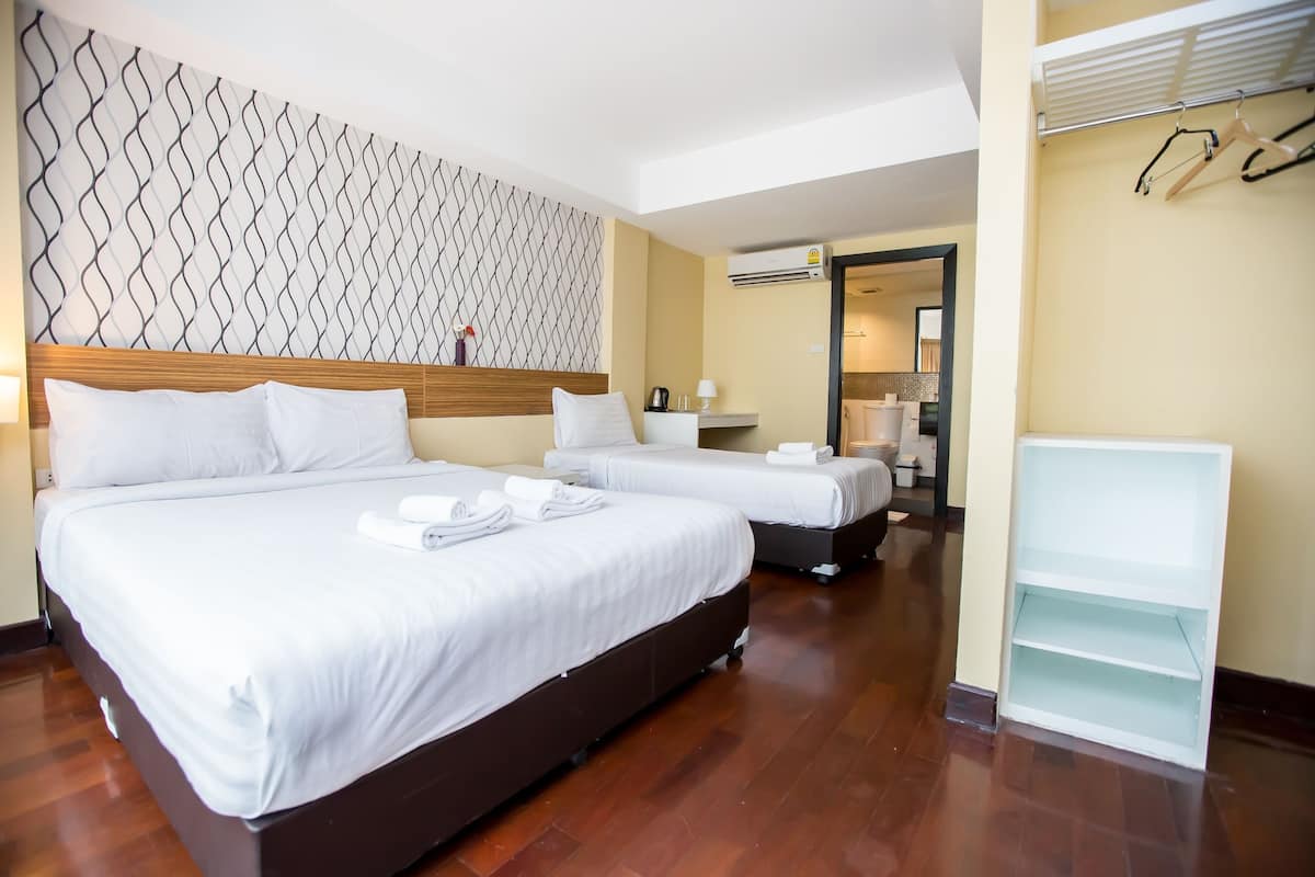 Una habitación de hotel con dos camas, un cabecero de madera, un papel tapiz estampado, un estante blanco y un equipo de aire acondicionado.