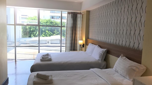 Een hotelkamer met twee bedden, een groot raam, een behang met patroon en een nachtkastje met een lamp.