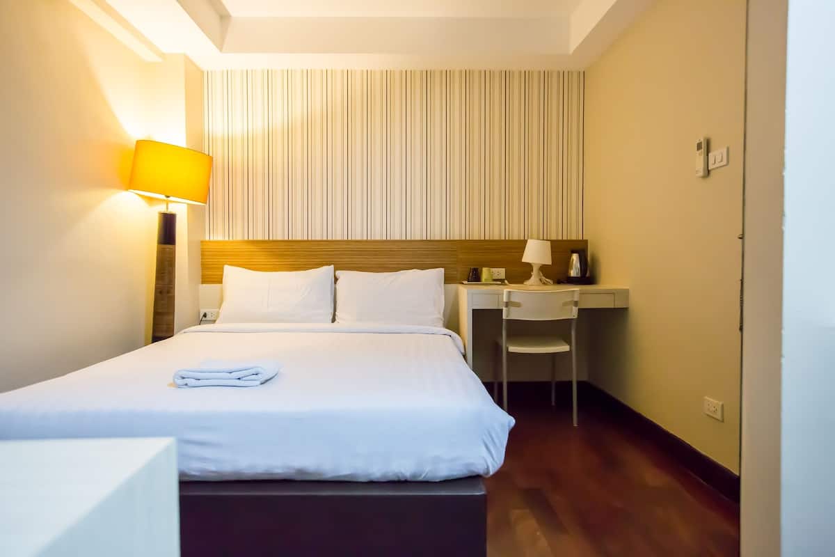 Una habitación de hotel con una cama bien hecha, un escritorio con una silla y una lámpara.