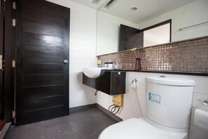 Een badkamer met een donker houten deur, witte betegelde wanden, een wit wastafelmeubel, een zwart kastje, een wit toilet en een betegelde spatwand.