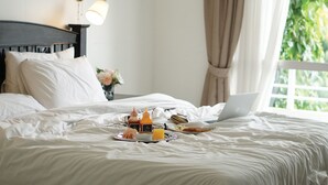 Un lit bien fait, avec un ordinateur portable, un plateau de petit-déjeuner et une bouteille d’eau.