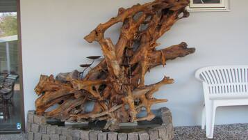 Una gran escultura de madera en una jardinera, una silla de plástico blanco y una ventana con vistas al exterior.