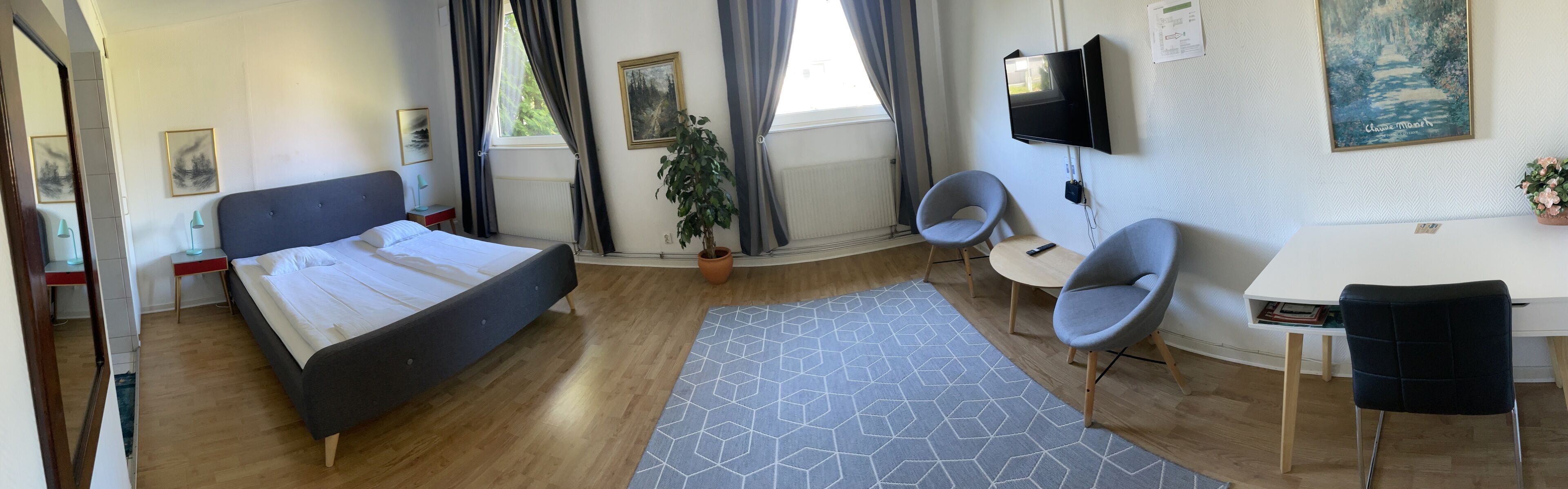 A modern bedroom with a bed, a desk, two chairs, a TV, and a window with curtains.