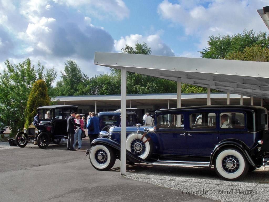 Vintage cars parked under a covered area with a building in the background.