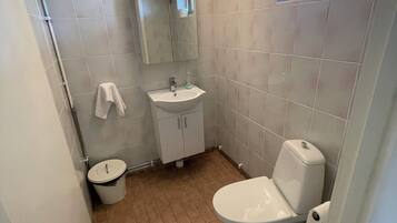 Un baño pequeño y funcional con un lavamanos, espejo y retrete blancos. Hay una ventana sobre el retrete y una toalla colgada en la pared.